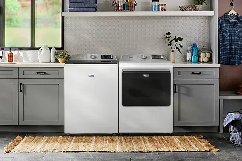 Maytag white top load agitator washing machine with glass lid in a modern laundry room setting.